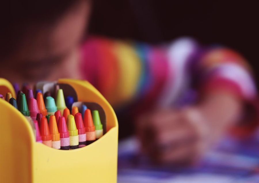 A child colouring with a pot of wax crayons